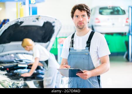 Maschio e femmina team meccanico esaminare auto a motore con la luce e la lista di controllo in officina Foto Stock