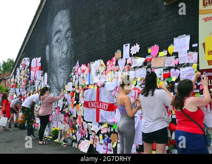 La gente lascia fiori e centinaia di note di supporto, immagini, bandiere e messaggi anti-razzisti sul gigante giocatore britannico di Manchester Marcus Rashford murale a Withington, Manchester, Inghilterra, Regno Unito, che è stato vandalizzato con graffiti abusivi dopo la perdita di calcio in Inghilterra Euro2020 l'11 luglio 2021. Il murale è stato creato dall'artista di strada francese Akse P19 sulla parete del Coffee House Cafe in Copson Street. Marcus Rashford è un calciatore del Manchester United. Akse riparò completamente il murale danneggiato entro il 13 luglio 2021. Data immagine: 13 luglio 2021. Foto Stock