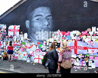 La gente lascia fiori e centinaia di note di supporto, immagini, bandiere e messaggi anti-razzisti sul gigante giocatore britannico di Manchester Marcus Rashford murale a Withington, Manchester, Inghilterra, Regno Unito, che è stato vandalizzato con graffiti abusivi dopo la perdita di calcio in Inghilterra Euro2020 l'11 luglio 2021. Il murale è stato creato dall'artista di strada francese Akse P19 sulla parete del Coffee House Cafe in Copson Street. Marcus Rashford è un calciatore del Manchester United. Akse riparò completamente il murale danneggiato entro il 13 luglio 2021. Data immagine: 13 luglio 2021. Foto Stock