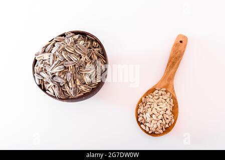 Semi di girasole sbucciati e grezzi in cucchiaio di legno isolato su fondo bianco. Foto Stock