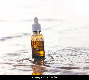 Siero cosmetico della pelle in contagocce di vetro. Pipettare il flacone in acqua con increspature. Concetto di ingredienti naturali SPA, essenza della pelle sullo sfondo del mare Foto Stock