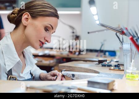 Gioielleria che lavora con attrezzi su un pezzo di gioielli al suo banco da lavoro Foto Stock