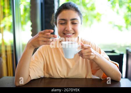 Sorridente giovane donna indiana che beve caffè al bar esterno Foto Stock