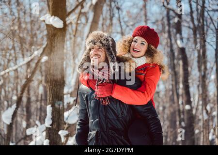 Uomo che porta la sua donna piggyback in una giornata invernale in modo gioioso, hanno divertimento in questa stagione Foto Stock