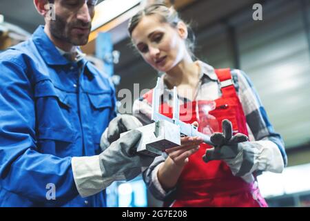 Donna e uomo soddisfatti che controllano le misure del pezzo metallico Foto Stock