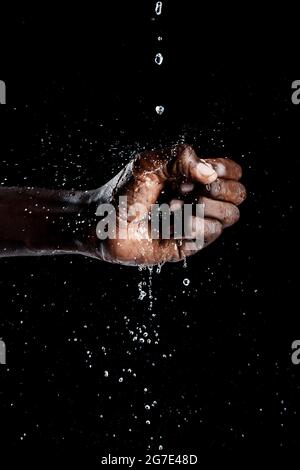 Mano dell'uomo africano che interagisce con l'acqua e sfondo nero. Foto Stock