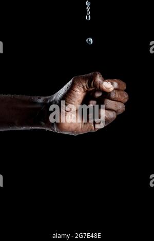 Mano dell'uomo africano che interagisce con l'acqua e sfondo nero. Foto Stock