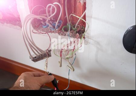 È stata aperta una scatola di derivazione del telefono: È stato collegato uno strumento di prova della linea con dei morsetti. Il tecnico controlla a mano gli altri cavi presenti. Foto Stock