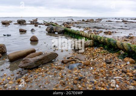 Una vecchia corda coperta di alghe si estende dal litorale al mare Foto Stock