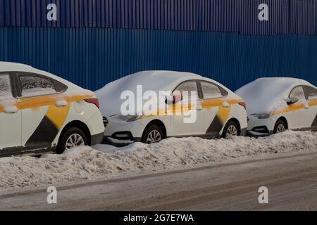 I taxi sono parcheggiati sulla strada in inverno. Auto coperte di neve. Le auto identiche vengono parcheggiate in fila. Trasporto in un bel parcheggio. Auto abbandonata shar Foto Stock