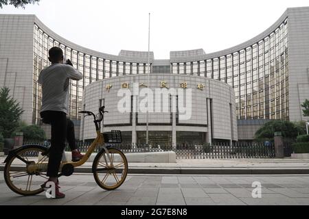 Pechino, Cina. 10 luglio 2021. Un uomo in bicicletta usa il suo cellulare per scattare una foto della sede della Banca popolare Cinese. La banca centrale cinese taglierà il coefficiente di riserva obbligatoria (RRR) di 0.5 punti percentuali a partire da luglio 15, rilasciando circa 1 trilione di yuan (154 miliardi di dollari) in liquidità per sostenere l'economia. Credit: SOPA Images Limited/Alamy Live News Foto Stock