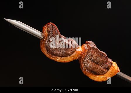 Bistecca al barbecue su spiedini su sfondo nero. Gastronomia brasiliana. Foto Stock