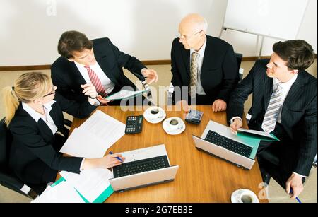 Il team aziendale discute di varie proposte e numeri incalcolanti mentre beve un sacco di caffè Foto Stock