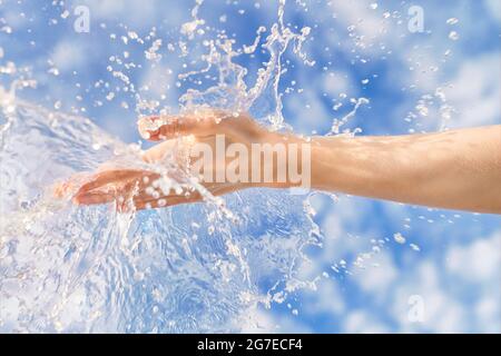 Donna mano con grande acqua spruzzare in esso contro cielo blu. Immagine estiva brillante, natura ed ecologia tema Foto Stock