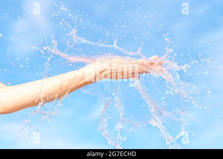 Donna mano con acqua spruzzare in esso contro il cielo blu. Immagine estiva brillante, natura ed ecologia tema Foto Stock