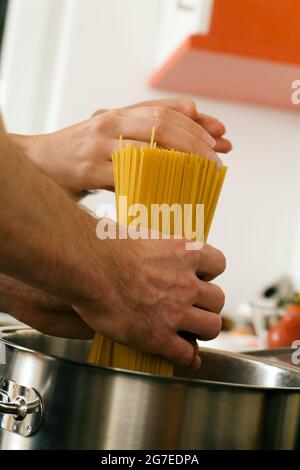 Coppia - solo le mani da vedere - cucinare la pasta, mettendo gli spaghetti in una pentola con acqua calda Foto Stock