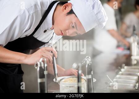 Giovani chef asiatico la placcatura di alimenti in un ristorante con attenzione il pipettaggio guarnire sul lato di una piastra Foto Stock