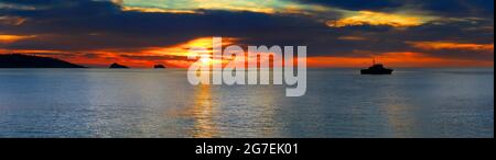 Vista panoramica sul mare con una barca e colline con un meraviglioso tramonto sullo sfondo, catturato nel rimorchio di Paignton, Devon - Inghilterra. Foto Stock