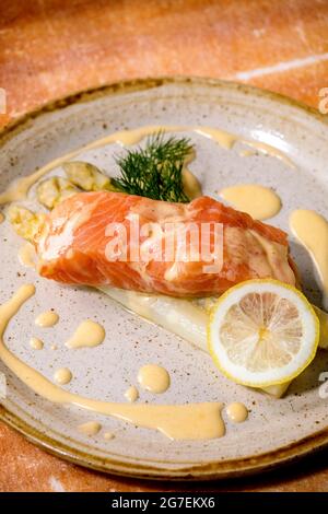 Pesce di salmone cotto su piatto di ceramica fatto in casa servito con asparagi bianchi, limone, aneto e salsa hollandaise su backgrpund di pietra arancio Foto Stock