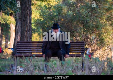 Timisoara, Romania - 10 ottobre 2020: Uomo seduto su una panchina in un parco. Persone reali. Foto Stock