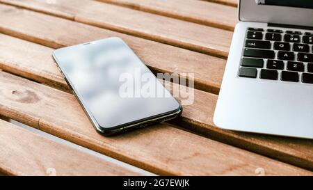 Smartphone mobile e computer portatile sulla scrivania con balcone in stile di lavoro da casa, messa a fuoco selettiva Foto Stock