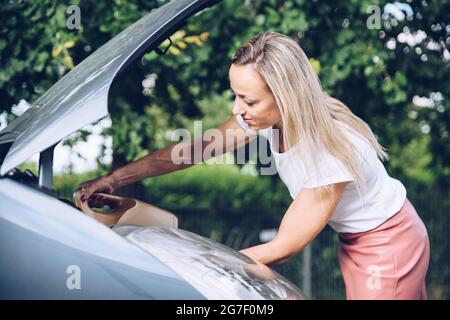 Donna che tiene la lattina di olio motore e la versa attraverso l'imbuto in auto. Foto Stock