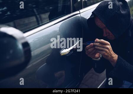 Ladro che si rompe in auto con picklock o cacciavite. Foto Stock