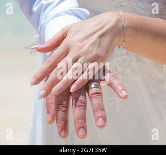 Vista closeup che mostra le mani di sposo e sposo coppia il giorno del matrimonio con anelli d'oro sulle dita durante la cerimonia estiva all'aperto Foto Stock