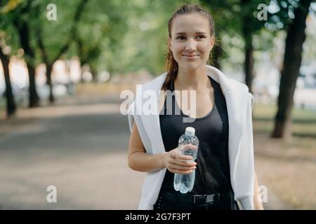 la giovane runner femminile tiene una bottiglia d'acqua all'aperto in abbigliamento attivo si rompe dopo l'allenamento passeggiate nel parco si rinfrescano dopo aver fatto jogging sensazione Foto Stock