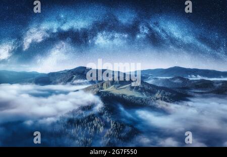 Arco della Via Lattea e montagne nelle nuvole basse nella notte stellata Foto Stock