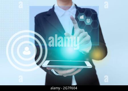 Donna in piedi uniforme che trasporta il telefono puntando sulle icone di display di interfaccia virtuale. Lady in Suit Holding Mobile Device indica l'innovazione Foto Stock