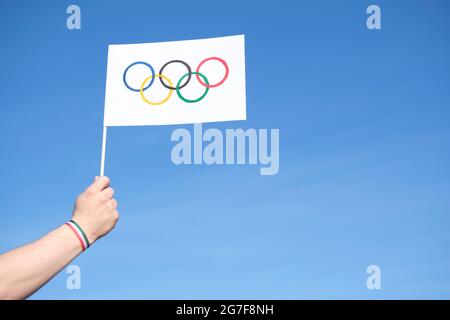 Mano che tiene una bandiera fatta a mano dei Giochi Olimpici all'aperto, contro un cielo limpido, con un bracciale verde, bianco e rosso, colori del Messico e nazionale Italia Foto Stock