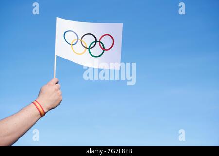 Mano che tiene una bandiera dei Giochi Olimpici fatti a mano all'aperto, contro un cielo limpido, con un bracciale spagnolo, rosso e giallo. Immagine con spazio di copia. Foto Stock