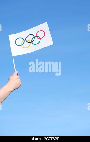 Mano che tiene una bandiera fatta a mano dei Giochi Olimpici all'aperto contro un cielo chiaro in una giornata di sole. Immagine con spazio di copia. Foto Stock