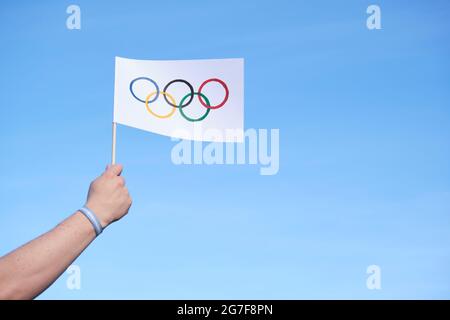 Mano che tiene una bandiera fatta a mano dei Giochi Olimpici all'aperto, contro un cielo limpido, con un bracciale argentino, blu chiaro e bianco. Immagine con spazio di copia. Foto Stock