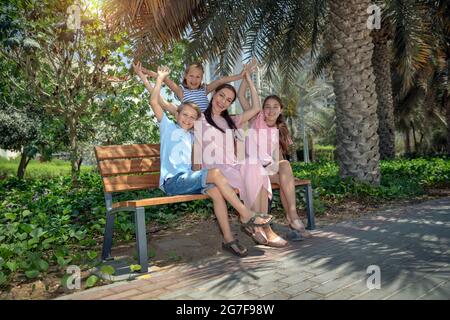 Madre felice e i suoi tre bambini preziosi seduti sul banco del Parco. Grande famiglia che si è bene a City Park il giorno d'estate. Concetto di amore. Foto Stock