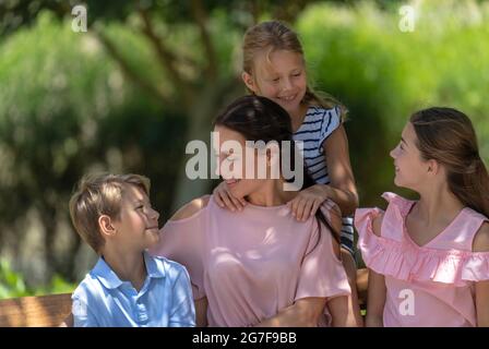 Ritratto di una grande famiglia felice all'aperto. Guardarsi l'uno sull'altro. Bella giovane Madre trascorrere il tempo con i suoi tre preziosi bambini. Foto Stock