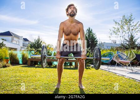 Uomo di mezza età che si adopera su crossfit e sollevamento pesi nel suo cortile Foto Stock