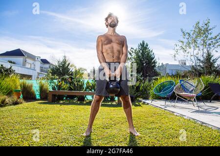 Uomo di mezza età che si adopera su crossfit e sollevamento pesi nel suo cortile Foto Stock