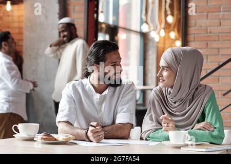 Uomo d'affari musulmano sorridente bearded che discute le carte con la donna in hijab mentre lavorano nel caffè Foto Stock