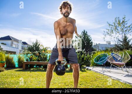 Uomo di mezza età che si adopera su crossfit e sollevamento pesi nel suo cortile Foto Stock