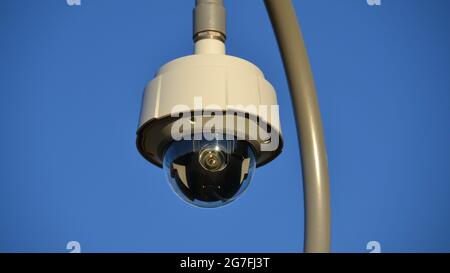 Vista ravvicinata di un TVCC a forma di cupola o di un obiettivo di una telecamera di sicurezza a circuito chiuso su un palo contro un cielo blu Foto Stock