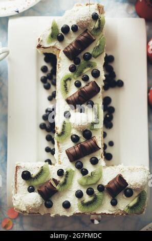 Colpo verticale di una torta a forma di numero uno con cioccolato, bacche e kiwi su un vassoio Foto Stock