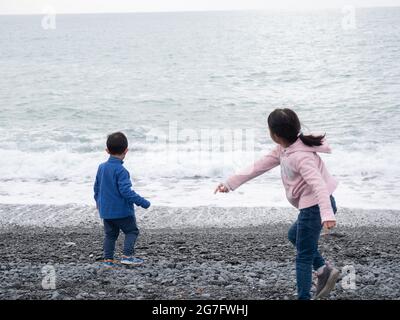 Vista posteriore dei bambini asiatici che gettano pietre nel mare Foto Stock