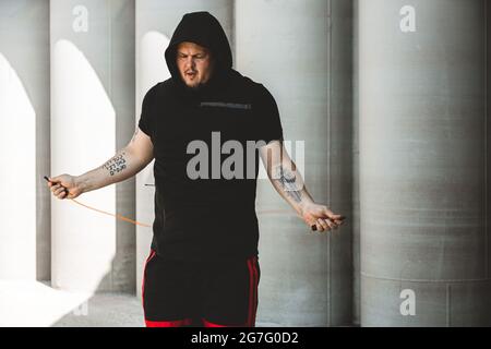 Uomo caucasico combattente allenarsi duramente all'aperto.. Uomo che usa la corda, che fa il warm up. Concetto di sport e pugilato Foto Stock