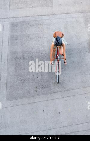 La ragazza snella in bicicletta corre in bicicletta lungo il marciapiede della città in cemento, preferendo uno stile di vita attivo e sano utilizzando il giro in bicicletta e il ciclo come un'alternativa Foto Stock