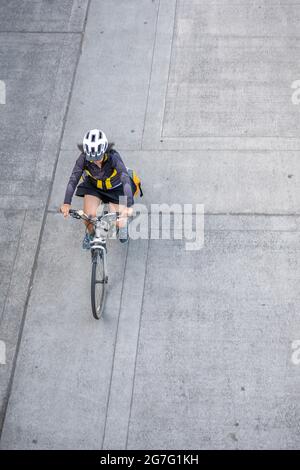 Una donna snella in bicicletta corre in bicicletta lungo il marciapiede della città in cemento, preferendo uno stile di vita attivo e sano utilizzando il giro in bicicletta e il ciclo come un al Foto Stock