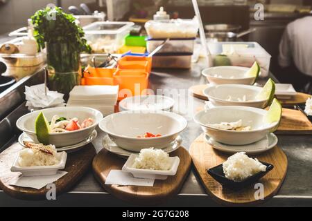 Chef professionisti che cucinano nel ristorante cucina dell'hotel, preparando la cena. Un cuoco in un grembiule fa un'insalata di verdure e pizza. Foto Stock