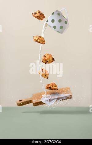 I biscotti equilibranti sopra il bordo di legno ed il latte che scorre fuori della tazza Foto Stock