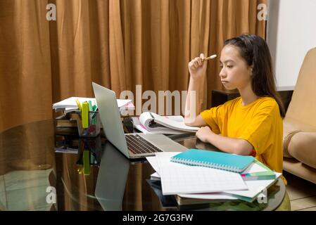 Bambina asiatica che fa il suo lavoro con il laptop a casa. Formazione online durante la quarantena Foto Stock